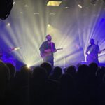 Publiek kijkt naar twee mannen op een podium.